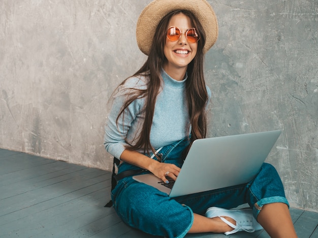 Portrait of creative young smiling woman in sunglasses. beautiful girl sitting on the floor near gray wall.