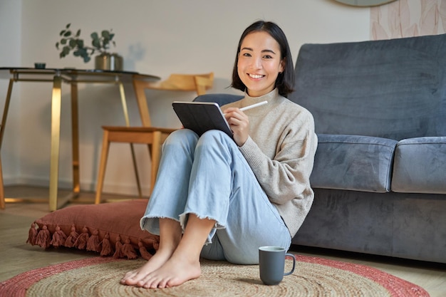 ホムから働くコーヒーを飲みながらペンでデジタル タブレットに描画する創造的な若い女性の肖像画