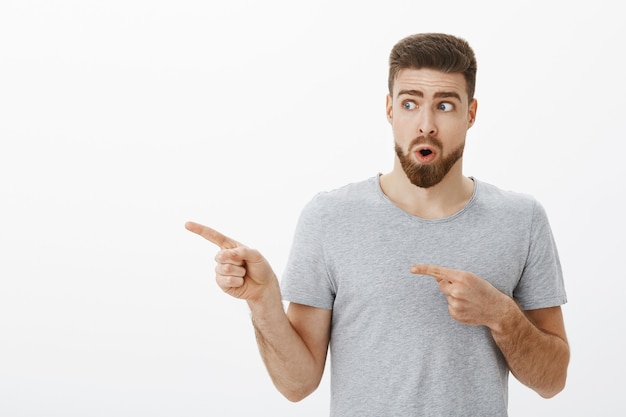 Portrait of curious and amazed good-looking charming male model with beard holding breat folding lips in wow sound looking and pointing left at cool hairstyle wanting same one while in barber shop