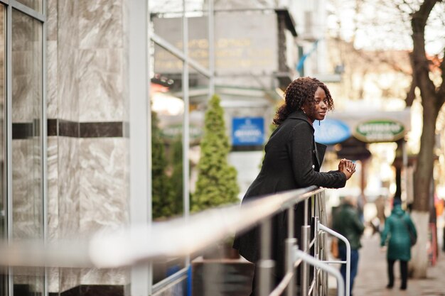 Portrait of a curly haired african woman wearing fashionable black coat and red turtleneck posing outdoor