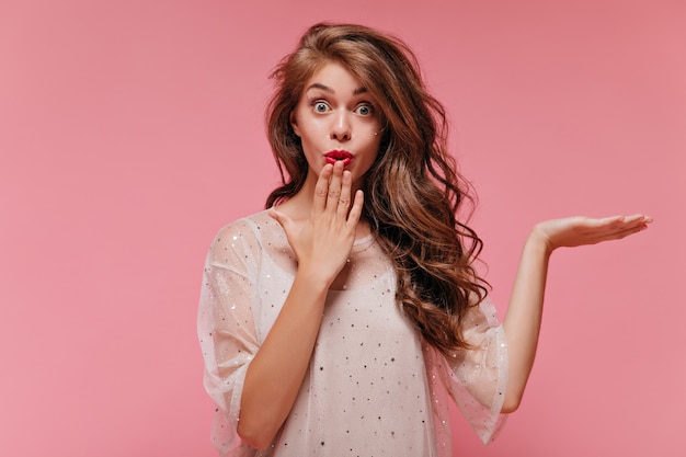 Portrait of curly long-haired woman in white stylish dress looking surprised