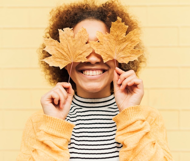 Free photo portrait of curly young woman covering her eyes with leaves