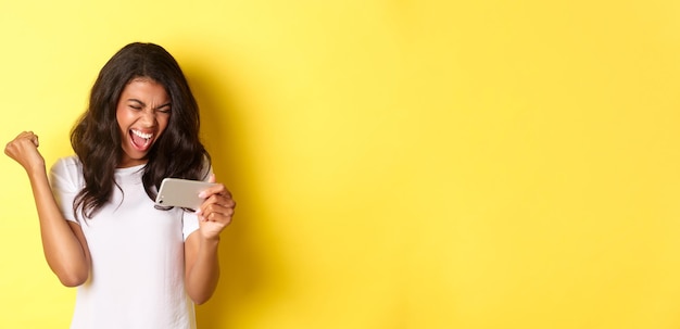 Free photo portrait of cute africanamerican girl winning in smartphone game shouting for joy making fist pump g