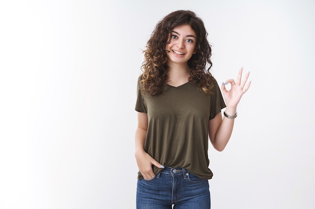 Portrait cute armenian curly-haired woman in olive t-shirt show okay gesture thinking outfit not bad agree say ok, smiling give approval confirm everything goes as planned, standing white background