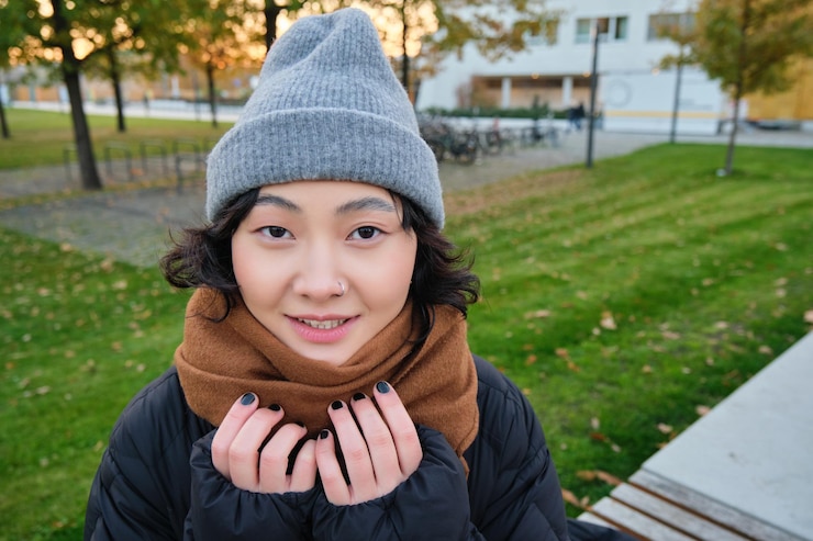 無料Photo 帽子とスカーフを着たかわいいアジアの女の子のポートレートは、肌寒い春の天候の笑顔とlで町を歩きます
