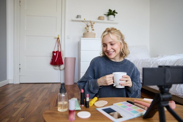 Portrait of cute blond woman video content maker vlogger recording on digital camera in bedroom