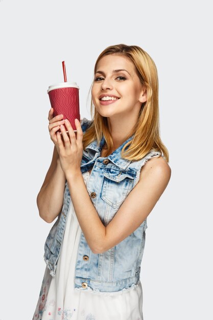 Portrait of cute blonde female in denim jacket with cup of coffee.