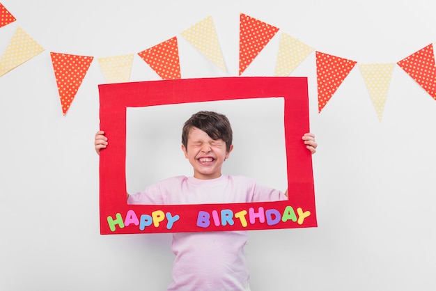 Portrait of a cute boy holding birthday frame with eyes closed