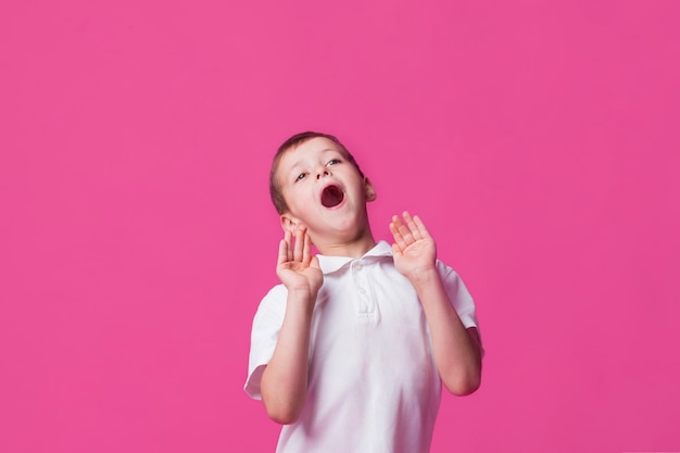 ピンクの背景に口を開けて叫んでいるかわいい男の子の肖像画