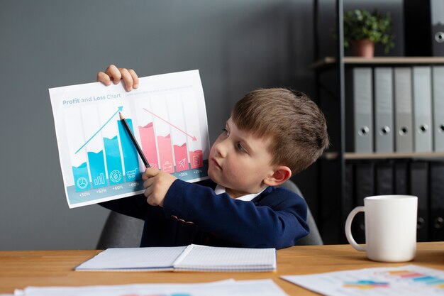 Portrait of cute boy showing graph at his office desk
