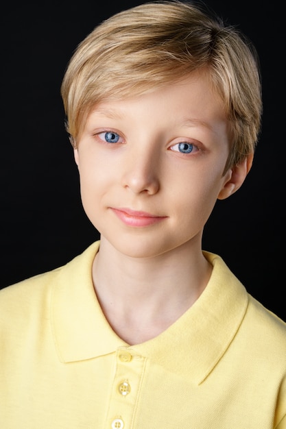 Portrait of a cute boy in a yellow t-shirt on a black background posing for the camera