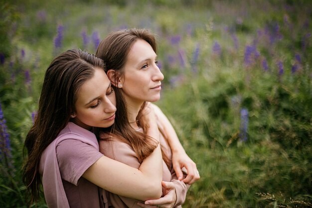 Portrait of cute caucasian brunette lesbian couple hugging on field with wild lupines