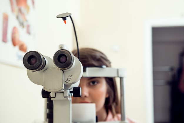 Ritratto del paziente femminile caucasico carino seduto in ufficio optometrista, in attesa di inizio della procedura per controllare la sua visione con il microbioscopio, seduto sul muro giallo. concetto di oftalmologia