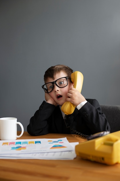 Portrait of cute child in suit using rotary phone at the office