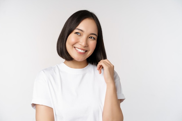 Free photo portrait of cute coquettish woman laughing and smiling looking aside thoughtful thinking or imaging smth standing in white tshirt over studio background