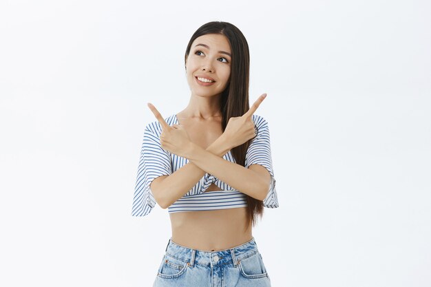 Portrait of cute and dreamy charming asian woman with cropped blouse crossing arms over chest pointing left