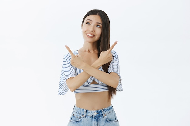 Portrait of cute and dreamy charming asian woman with cropped blouse crossing arms over chest pointing left