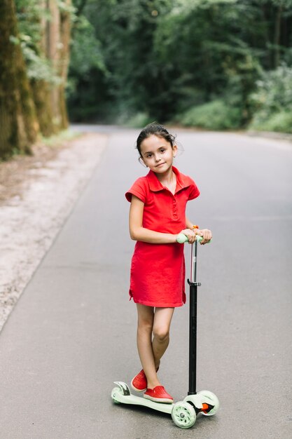 Portrait of a cute girl standing over scooters on road