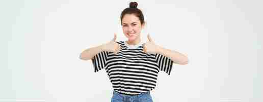 Free photo portrait of cute girl student shows thumbs up recommends product approves choice likes item stands