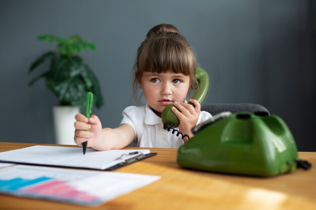 Portrait of cute girl using rotary phone at her office desk