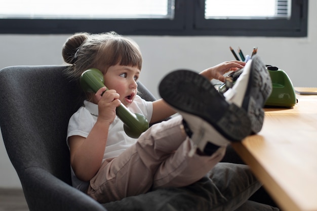 Portrait of cute girl using rotary phone at her office desk