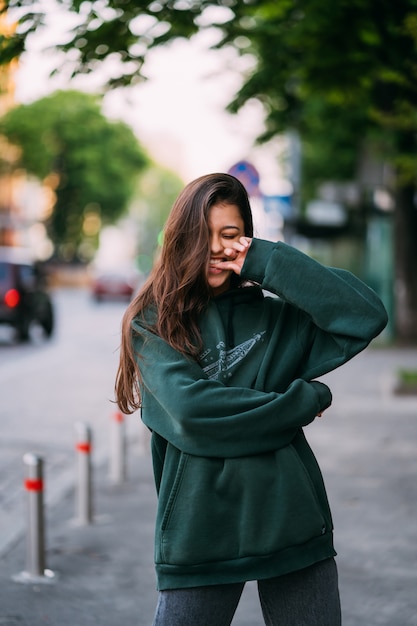 Portrait of cute girl with long hair looks at the camera in city on street background.