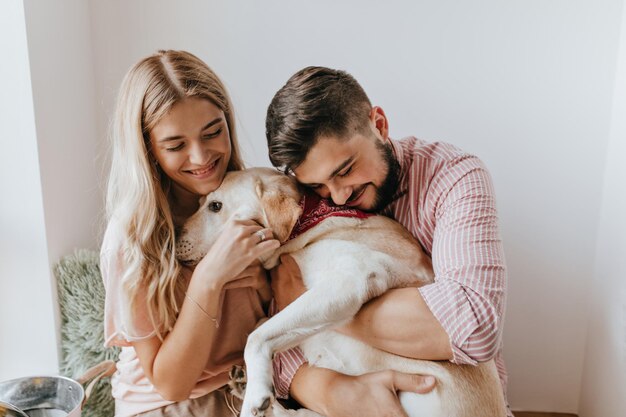 Portrait of cute guy and girlfriend with smile hugging Labrador with burgundy scarf around his neck