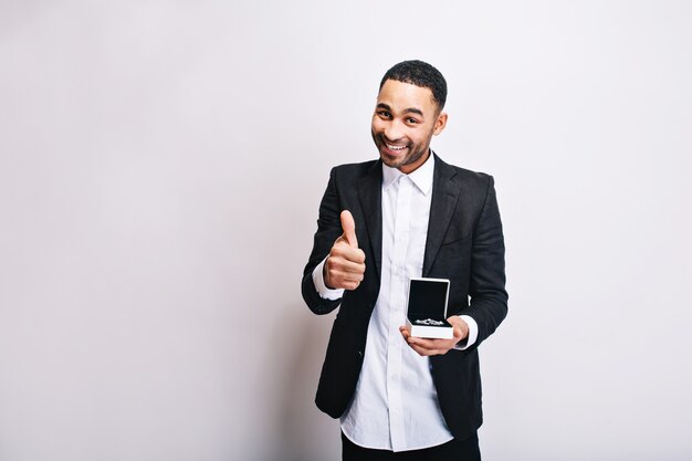 Portrait cute handsome guy in white shirt, black jacket with gift in hands smiling. Expressing true positive emotions, cheerful mood, present for girlfriend, jewellery.