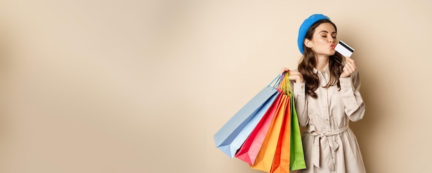 Free photo portrait of cute happy girl kissing her credit card after buying gifts holding shopping bags standin