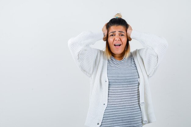 Portrait of cute lady keeping hands on head in t-shirt, cardigan and looking excited front view