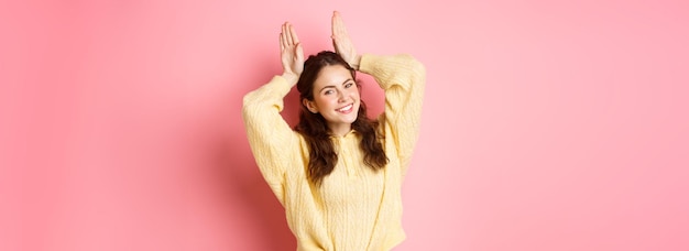 Free photo portrait of cute lady showing easter bunny ears gesture and smiling posing like silly rabbit standin