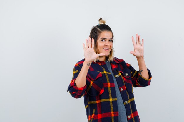 Portrait of cute lady showing surrender gesture in checked shirt and looking happy