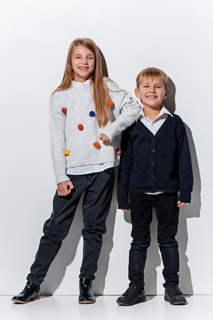 The portrait of cute little boy and girl in stylish jeans clothes looking at camera at studio