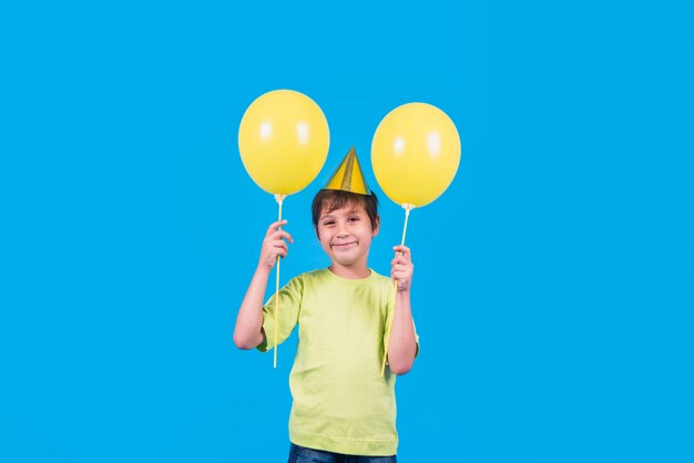 Portrait of a cute little boy holding yellow balloons against blue backdrop