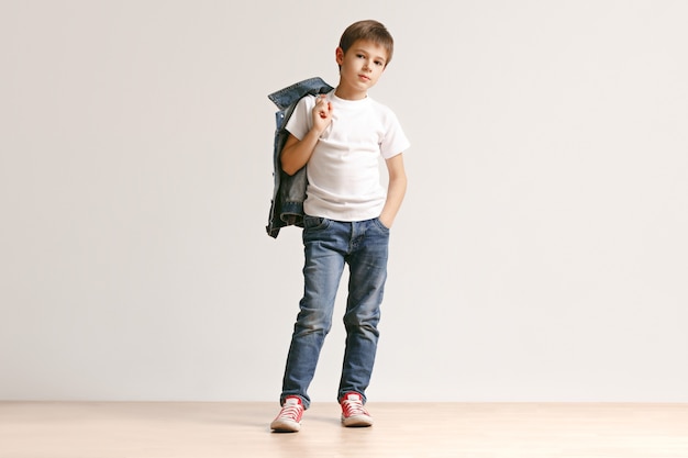 The portrait of cute little boy in stylish jeans clothes looking at camera at studio