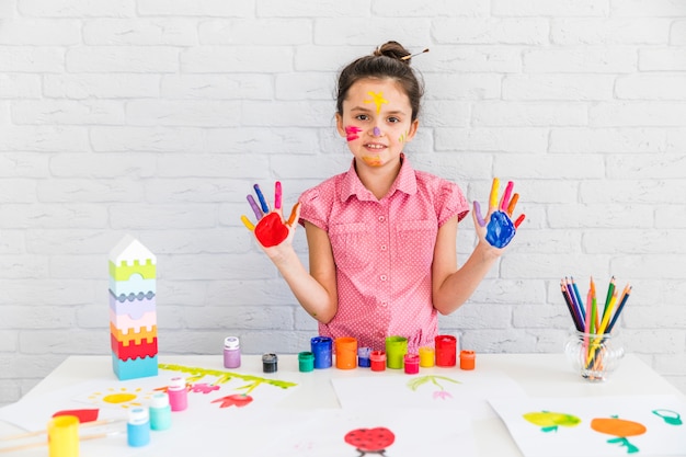 Portrait of cute little girl showing her painted hands standing against white brick wall