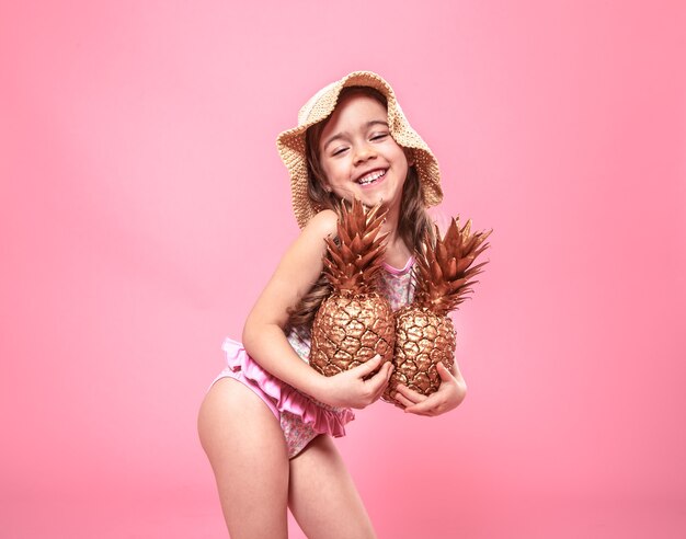 Portrait of a cute little girl in a summer hat, holding two pineapples painted in gold, the concept of summer and creativity