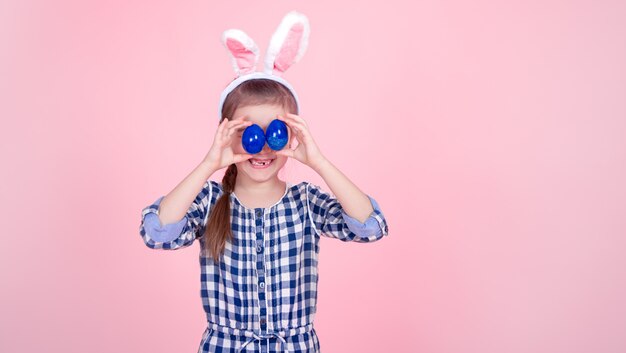 Free photo portrait of a cute little girl with easter eggs on a pink background.