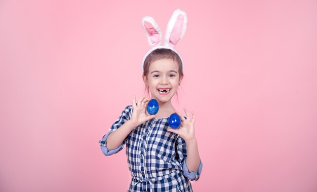 Portrait of a cute little girl with Easter eggs on a pink background.