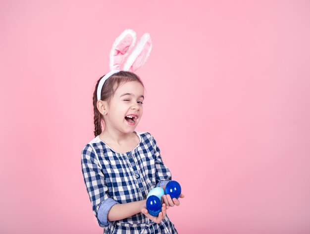 Портрет милой маленькой девочки с пасхальными яйцами на розовой предпосылке.