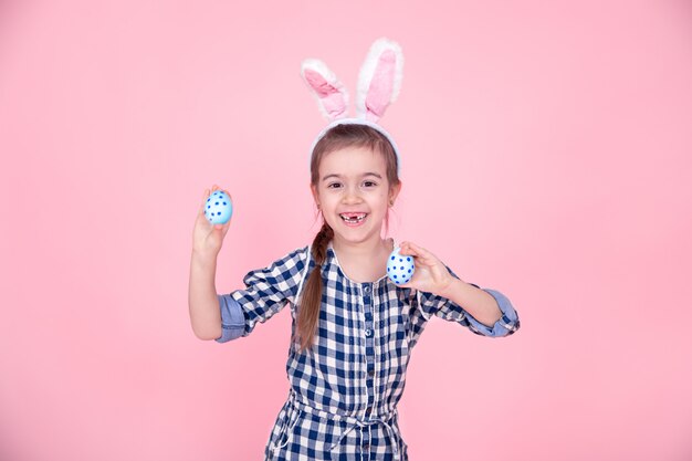 Portrait of a cute little girl with Easter eggs on a pink background.