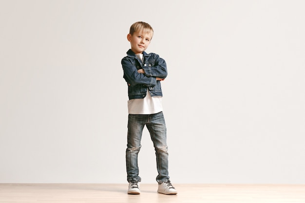 白いスタジオの壁に対してカメラを見てスタイリッシュなジーンズの服でかわいい子供男の子の肖像画。キッズファッションコンセプト