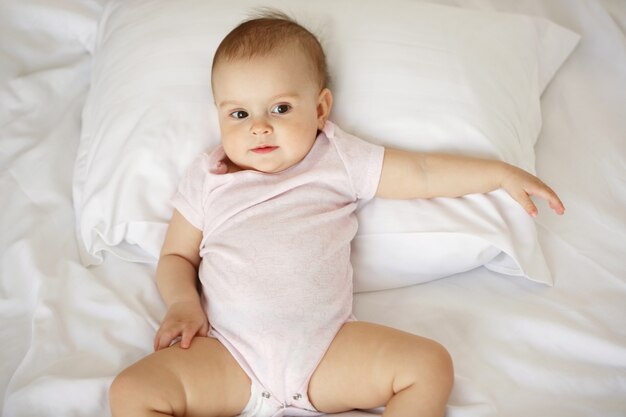 Portrait of cute nice little baby woman lying on pillow in bed. From above.