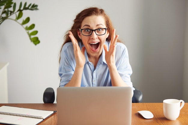 Portrait of a cute redhead girl wearing glasses and blue shirt screaming with excitement