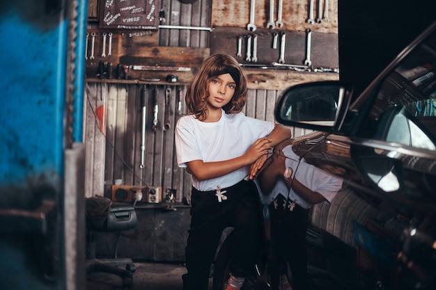 Free photo portrait of cute small girl near shiny car at atuo service workshop.