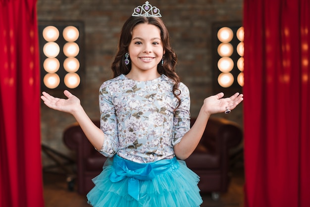 Free photo portrait of cute smiling girl wearing crown standing in studio