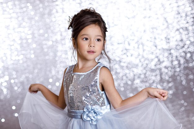 Portrait of cute smiling little child girl in princess dress on background with silver bokeh. birtday party