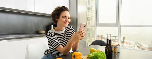 Portrait of cute smiling woman cooking salad looking at smartphone watching recipe food preparation