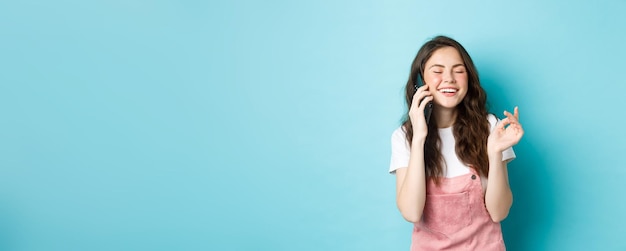 Free photo portrait of cute and stylish girl laughing while chatting on phone holding smartphone near ear and s