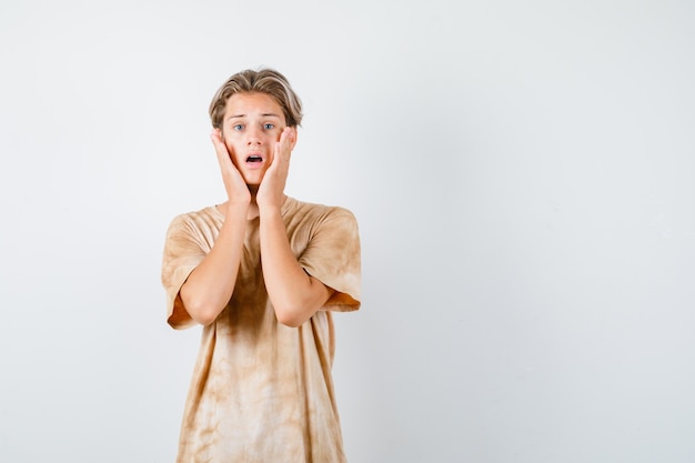 Portrait of cute teen boy keeping hands on cheeks in t-shirt and looking anxious front view